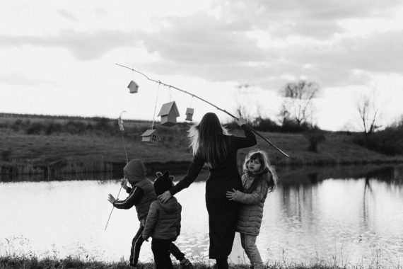 A mother and her children enjoy a serene moment at a lakeshore, captured in black and white.