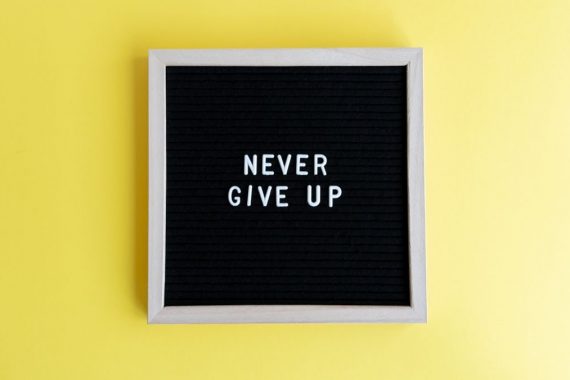 Black felt board with 'Never Give Up' on a bright yellow background for motivation.